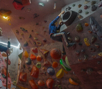 Ein Mann schaut einem Jungen beim Klettern an einer Boulderwand zu.