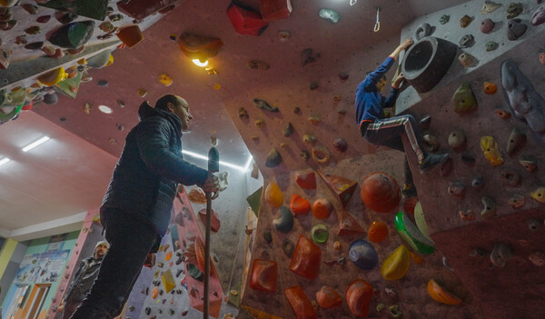 A man watches a boy climbing on a bouldering wall.