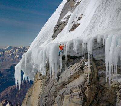 Mann klettert in hoher Luft an einem Beg mit Schnee undd Eiszapfen