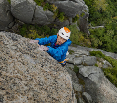 Sachi Amma, mit gelb-orangenem Helm und blauer Outdoor-Jacke, in Nahaufnahme, wie er einen Berg klettert