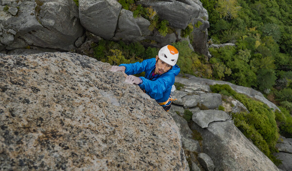 Sachi Amma, mit gelb-orangenem Helm und blauer Outdoor-Jacke, in Nahaufnahme, wie er einen Berg klettert